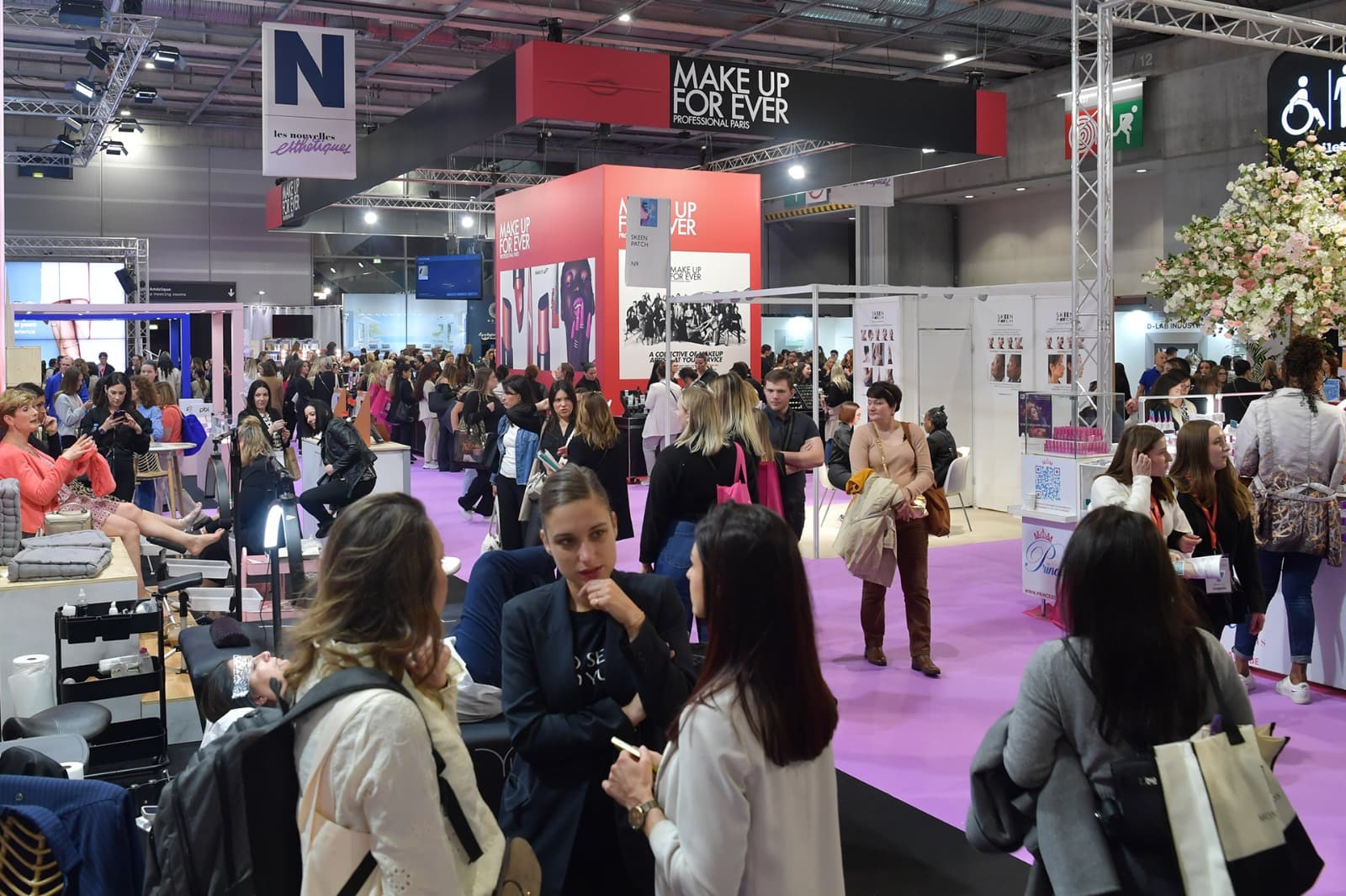 Allée d'un salon professionnel de la beauté remplie de visiteuses entre les stands